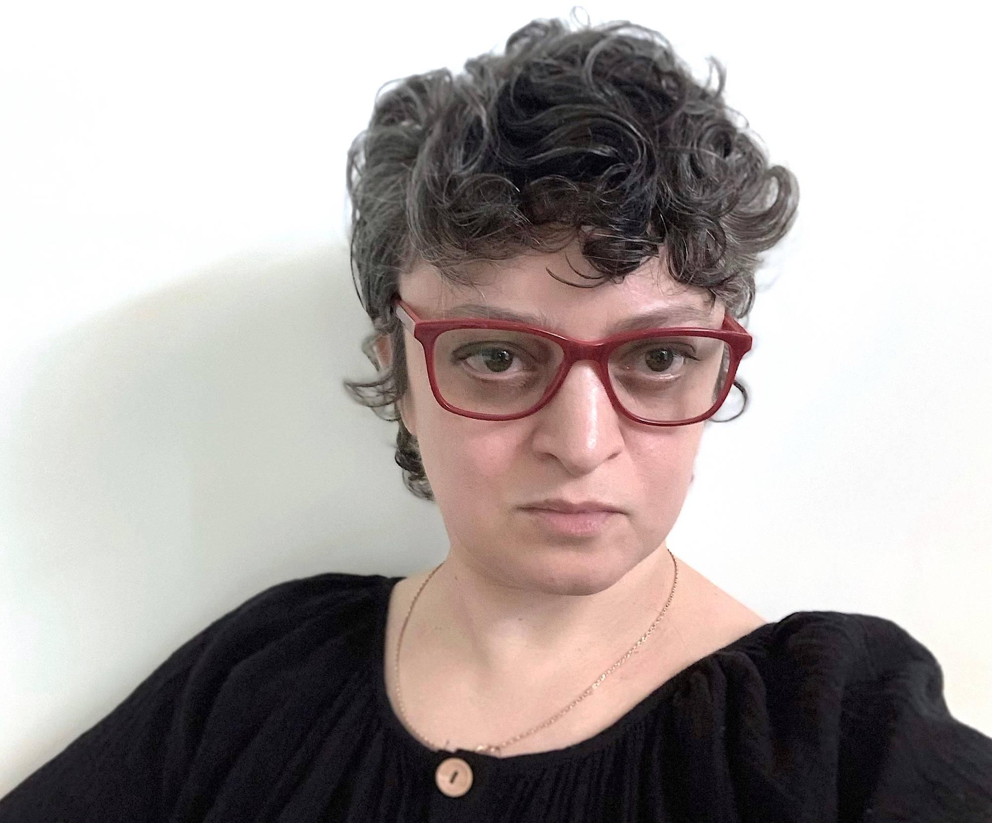 Image of Katya Grokhovky wearing red glasses & black shirt.